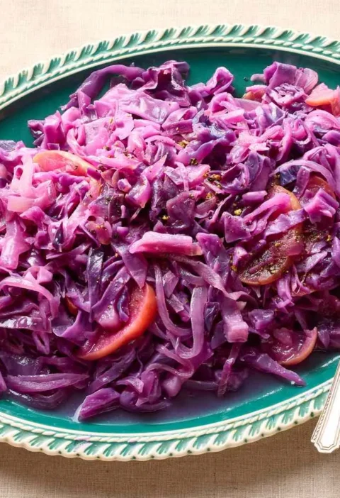 Martha Stewart braised red cabbage with apple and onion served on a green oval platter with a serving spoon