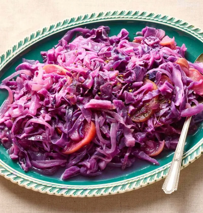 Martha Stewart braised red cabbage with apple and onion served on a green oval platter with a serving spoon