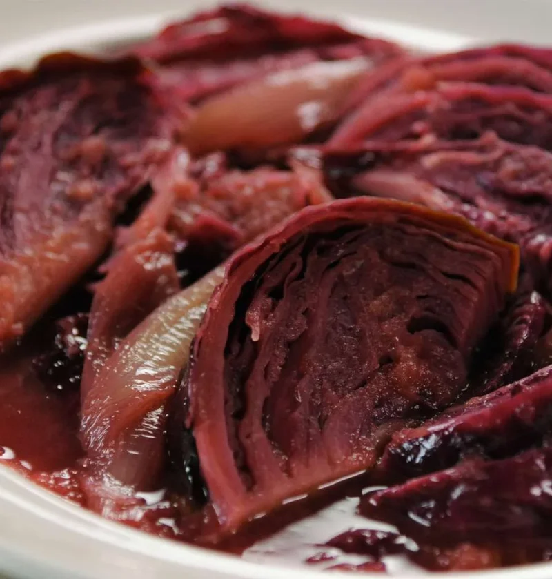 Martha Stewart braised red cabbage with caramelized apples and onion wedges in a glossy syrup on a white plate