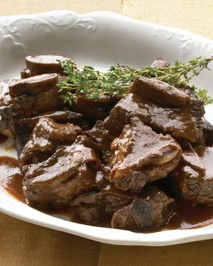 Martha Stewart braised short ribs in glossy red wine sauce on a white plate garnished with fresh thyme sprigs