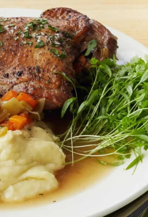 Martha Stewart braised turkey legs on a white plate with leeks and carrots, mashed potatoes and fresh herb greens