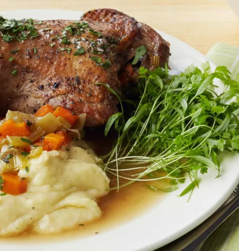 Martha Stewart braised turkey legs on a white plate with leeks and carrots, mashed potatoes and fresh herb greens