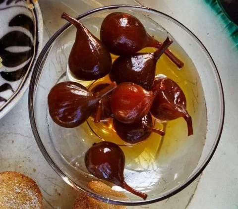 Martha Stewart brandied figs with stems in golden syrup in a glass bowl next to pistachio truffles and sugar-dusted cookies