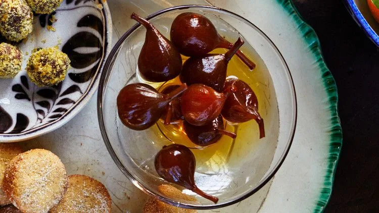 Martha Stewart brandied figs with stems in golden syrup in a glass bowl next to pistachio truffles and sugar-dusted cookies