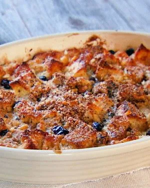 Martha Stewart bread pudding with rum sauce in an oval baking dish, golden brown bread cubes with raisins and a crumb topping