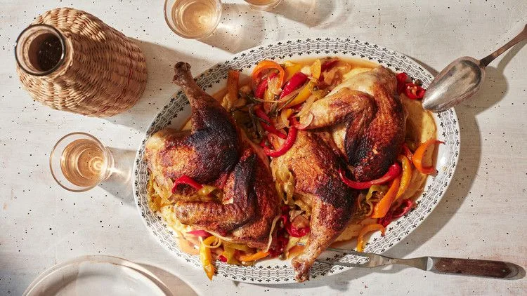 Martha Stewart brick chicken with vinegar peppers, two crispy chicken halves on a platter of sliced red and yellow peppers