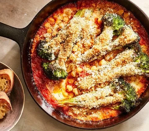 Martha Stewart Broccoli-and-Chickpea Parmesan in a cast-iron skillet with roasted broccoli, chickpeas, marinara and a golden panko topping, toasted bread beside it