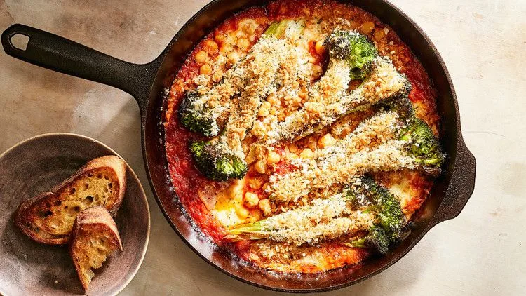 Martha Stewart Broccoli-and-Chickpea Parmesan in a cast-iron skillet with roasted broccoli, chickpeas, marinara and a golden panko topping, toasted bread beside it