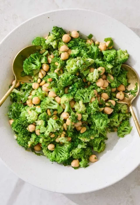 Martha Stewart broccoli and chickpea salad in a white bowl with gold serving spoons