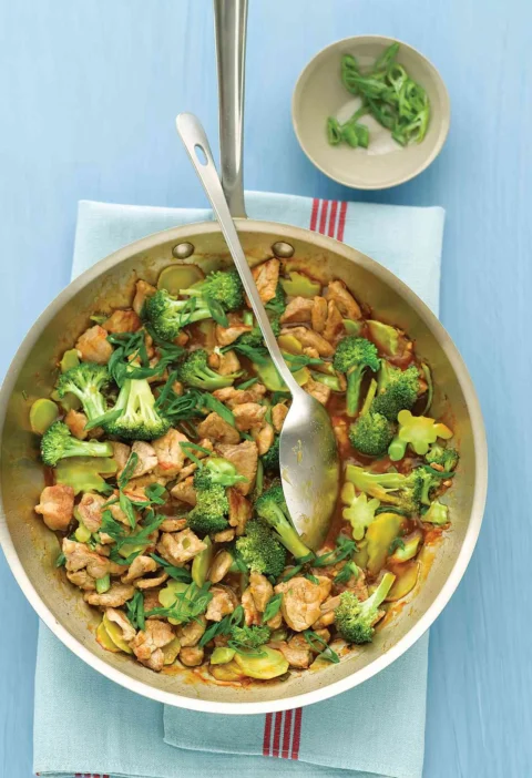 Martha Stewart broccoli and pork stir-fry in a stainless steel skillet with sliced scallions on top
