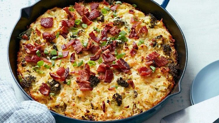 Martha Stewart broccoli-cheddar hash-brown casserole topped with crumbled bacon and sliced scallions in a cast iron skillet