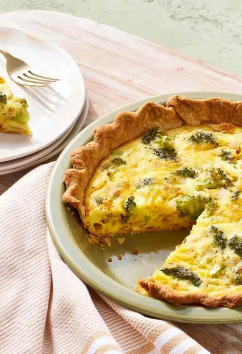 Martha Stewart broccoli-cheddar quiche in a green pie plate with one slice served on a white plate