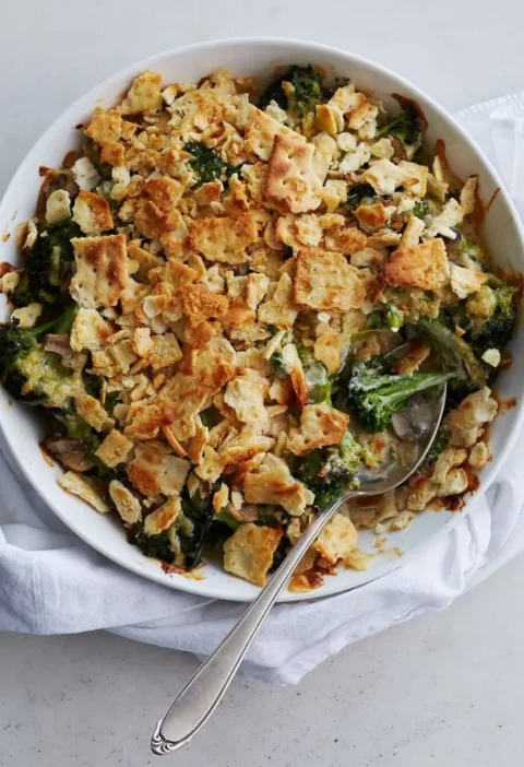 Martha Stewart broccoli cheese casserole with crackers in a white bowl, topped with golden crushed saltines and served with a spoon