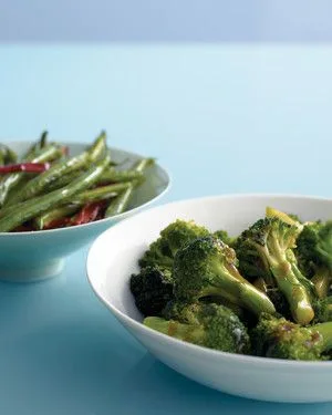 Martha Stewart broccoli with oyster sauce in a white bowl next to a bowl of green beans on a blue table