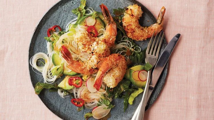 Broiled coconut-and-lime-crusted shrimp over a rice-noodle salad with avocado, radishes and red chile slices on a dark plate