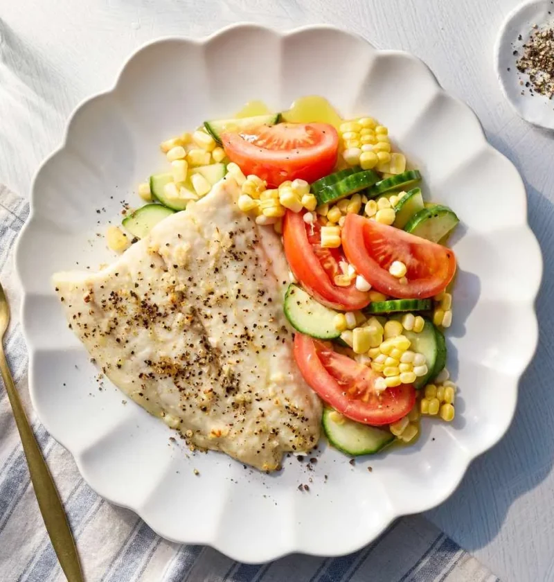 Martha Stewart broiled fish with summer salad, a peppered flounder fillet beside tomato wedges, cucumber and corn on a white scalloped plate
